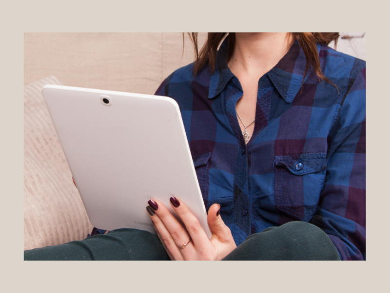 Photo of woman in blue and black check shirt reading news on a white tablet device .